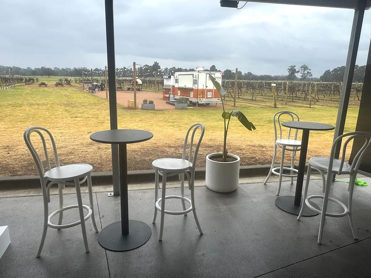 Black Atlas bar tables with white bentwood bar stools set up under cover at a vineyard event.