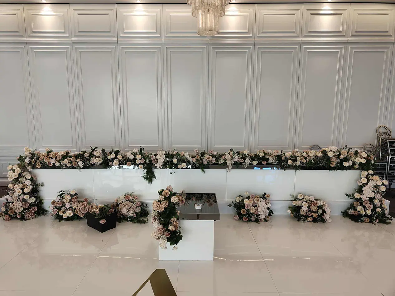 White bridal table with soft pink and white floral arrangements in an elegant wedding reception venue with decorative wall panelling