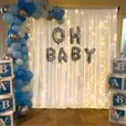 White draping with warm fairy lights, blue and silver balloon garland and baby shower balloon lettering for a styled celebration display