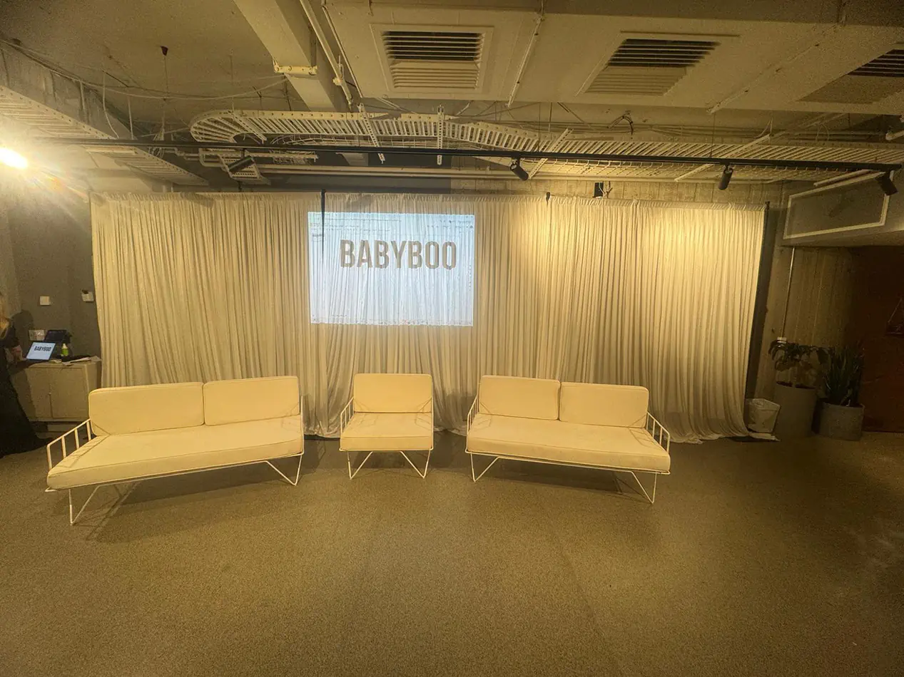 White draping behind white lounge seating, with a projected logo display and matching event furniture in an indoor venue