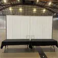 White draping behind two black-covered tables and chairs in a large exhibition or warehouse-style event space