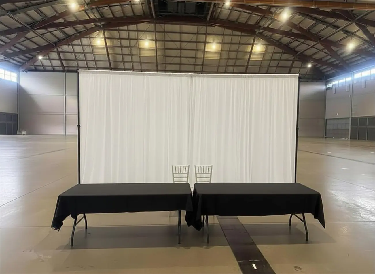 White event draping backdrop positioned behind black registration tables inside a large exhibition venue