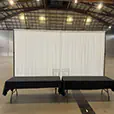 White event draping backdrop positioned behind black registration tables inside a large exhibition venue