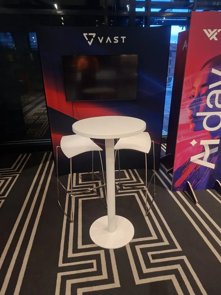 White exhibition stools arranged around a white Atlas bar table at an indoor event