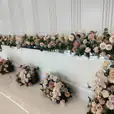 White gloss bridal table featuring elegant floral décor in soft neutral tones, with roses, orchids, and greenery styled for a modern wedding reception.