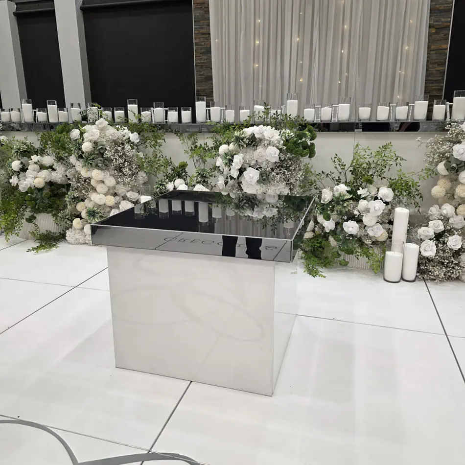 White gloss cake table positioned on a white dance floor with elegant floral arrangements and candle backdrop at a wedding reception