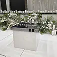 White gloss cake table positioned on a white dance floor with elegant floral arrangements and candle backdrop at a wedding reception