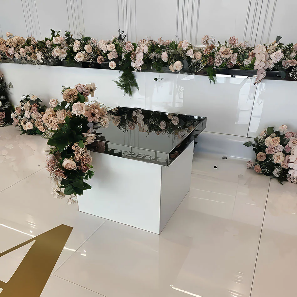 Mirror gloss cake table with reflective black surface, surrounded by lush white and green floral arrangements and rows of tall candles at a wedding reception.