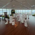 White illuminated stools and cocktail tables arranged in a modern indoor event space with timber flooring and city views through large windows