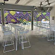 White hairpin bar tables with white wire chairs set in a modern indoor venue featuring a large green wall and open event layout