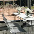 A white hairpin high bar table set up with white chairs and flowers.