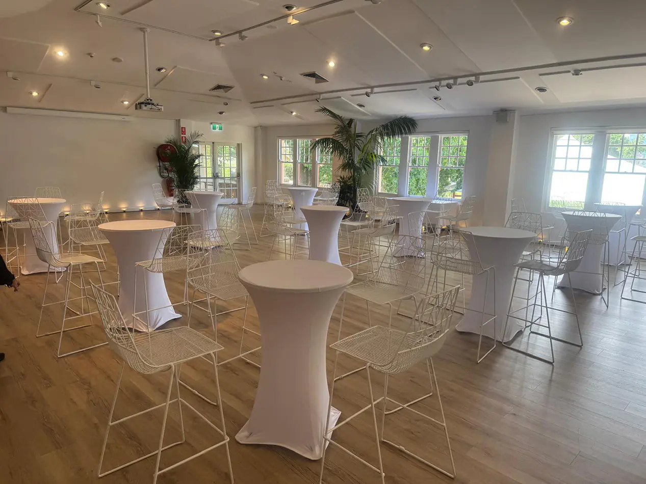 White lycra cocktail tables with matching white wire stools arranged throughout a modern indoor event space