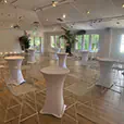 White lycra cocktail tables with matching white wire stools arranged throughout a modern indoor event space