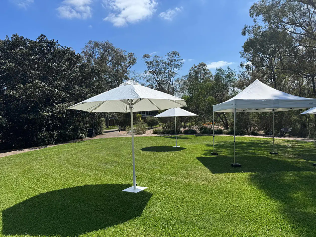White market umbrella set up on grass in an outdoor garden space providing shade for an event area