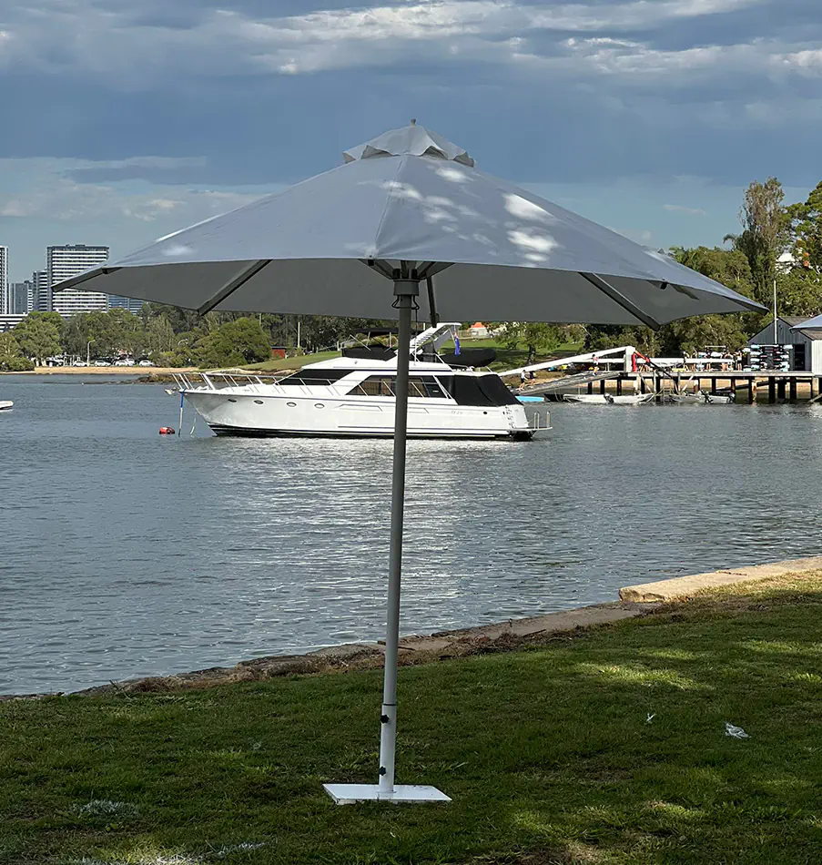 White market umbrella providing shade beside a waterfront with boats and trees in the background on a sunny day