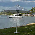 White market umbrella providing shade beside a waterfront with boats and trees in the background on a sunny day