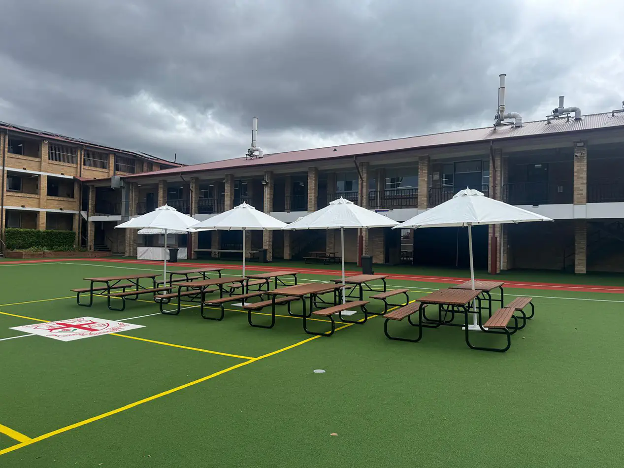 Multiple white market umbrellas providing shade over picnic tables in a school courtyard setting with open outdoor space
