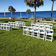 White padded folding chairs arranged on grass for a beachfront outdoor ceremony with ocean views and palm trees