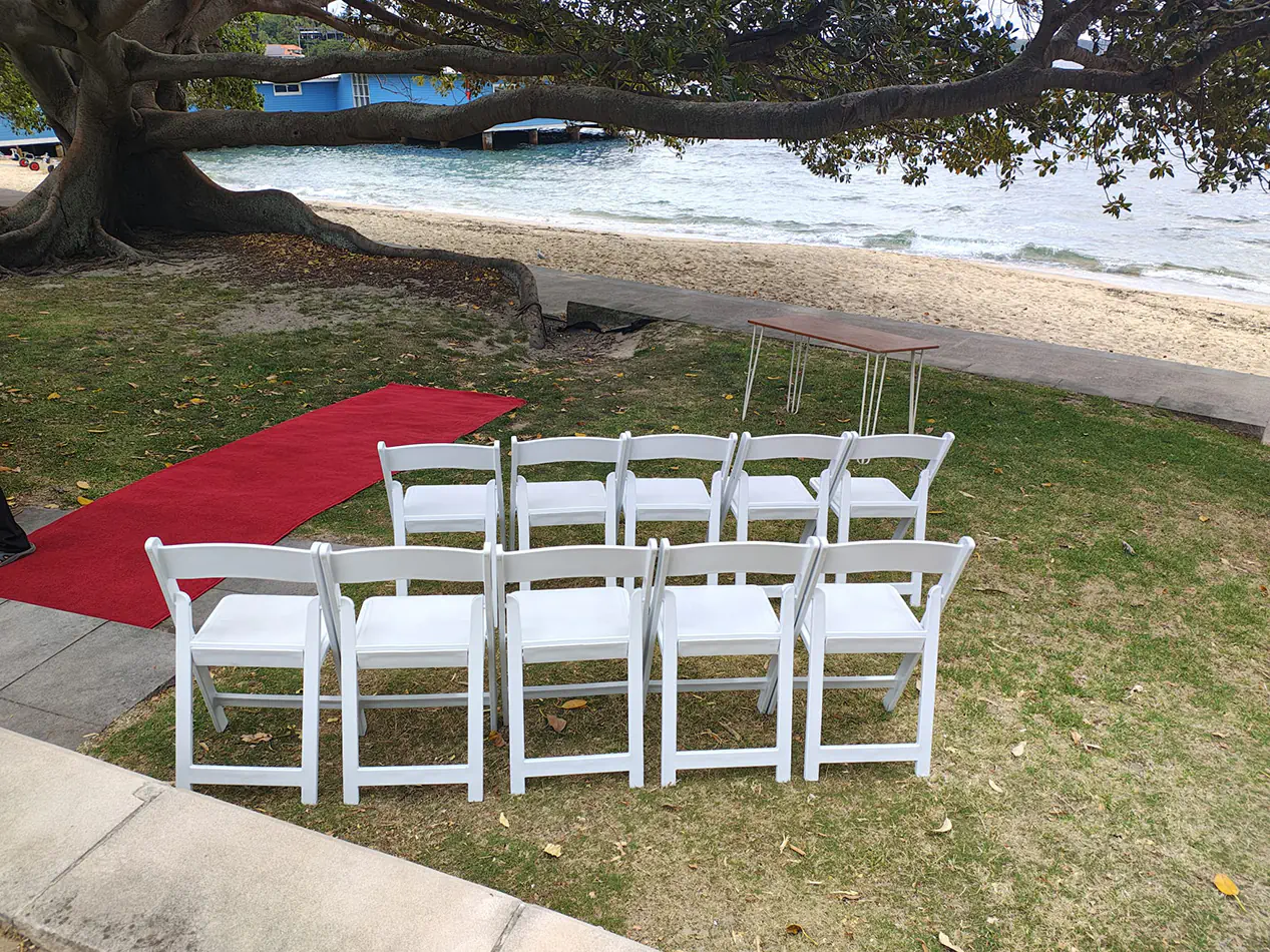 White padded folding chairs arranged beside a red carpet aisle for a waterfront wedding ceremony setup