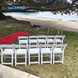White padded folding chairs arranged beside a red carpet aisle for a waterfront wedding ceremony setup