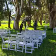 A wedding ceremony set up in the middle of a grassy field. The couple exchanged vows surrounded by white padded folding chairs, creating an elegant and stylish ambiance amidst the natural beauty of the outdoors