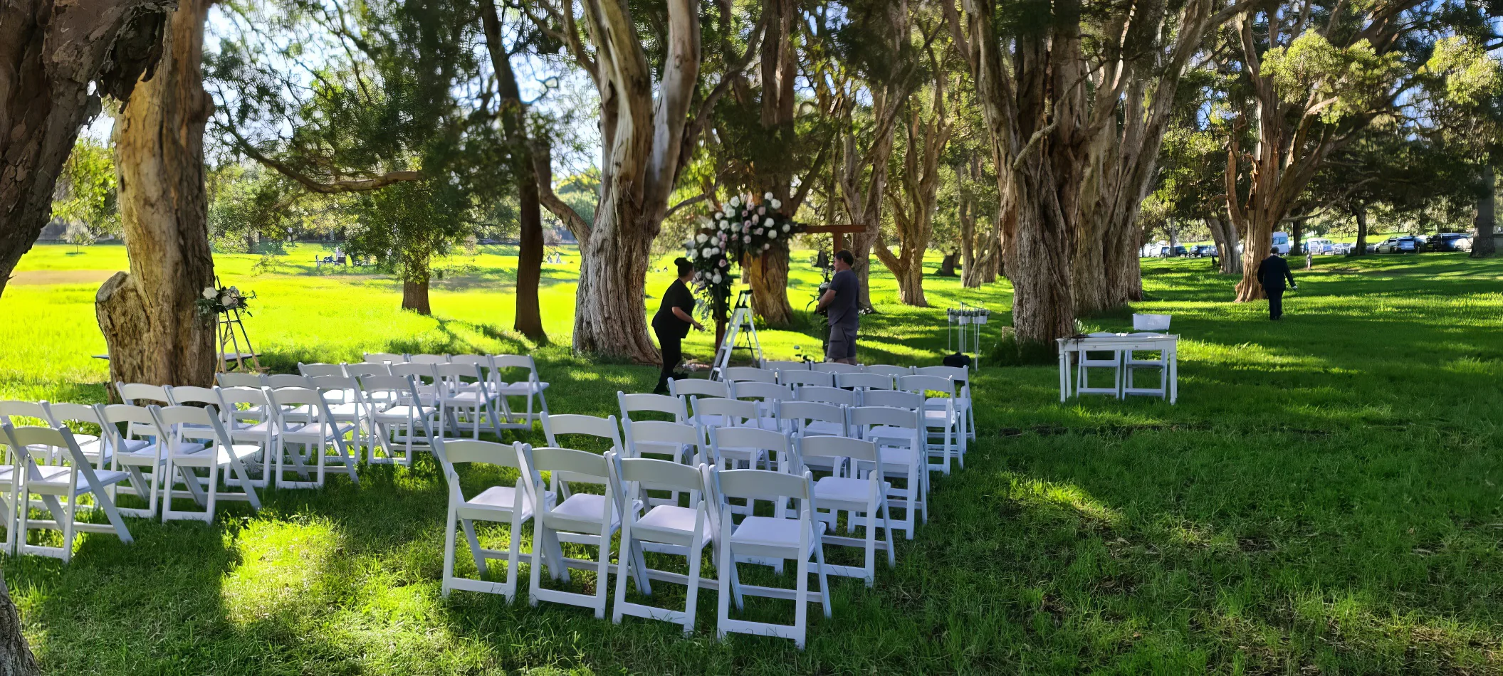 A wedding ceremony set up in the middle of a grassy field. The couple exchanged vows surrounded by white padded folding chairs, creating an elegant and stylish ambiance amidst the natural beauty of the outdoors