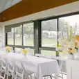 A long table is set up in a room with windows, decorated with elegant White Padded Folding Chair Hire (Gladiator chair).