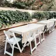 A white table and chairs set up on a wooden deck, including White Padded Folding Chairs (Gladiator chairs).