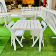 A white table and chairs on a green grass park setting. White padded folding chairs (Gladiator chair) available for hire.