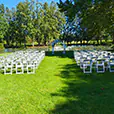White padded folding chairs arranged in rows on grass for an outdoor wedding ceremony beside a lake with floral arbour