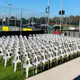 A large group of white plastic chairs on a grass field.