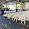 A gymnasium filled with white plastic stackable chairs and a basketball court.