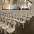 A large room full of white plastic stackable chairs in front of a rock wall.
