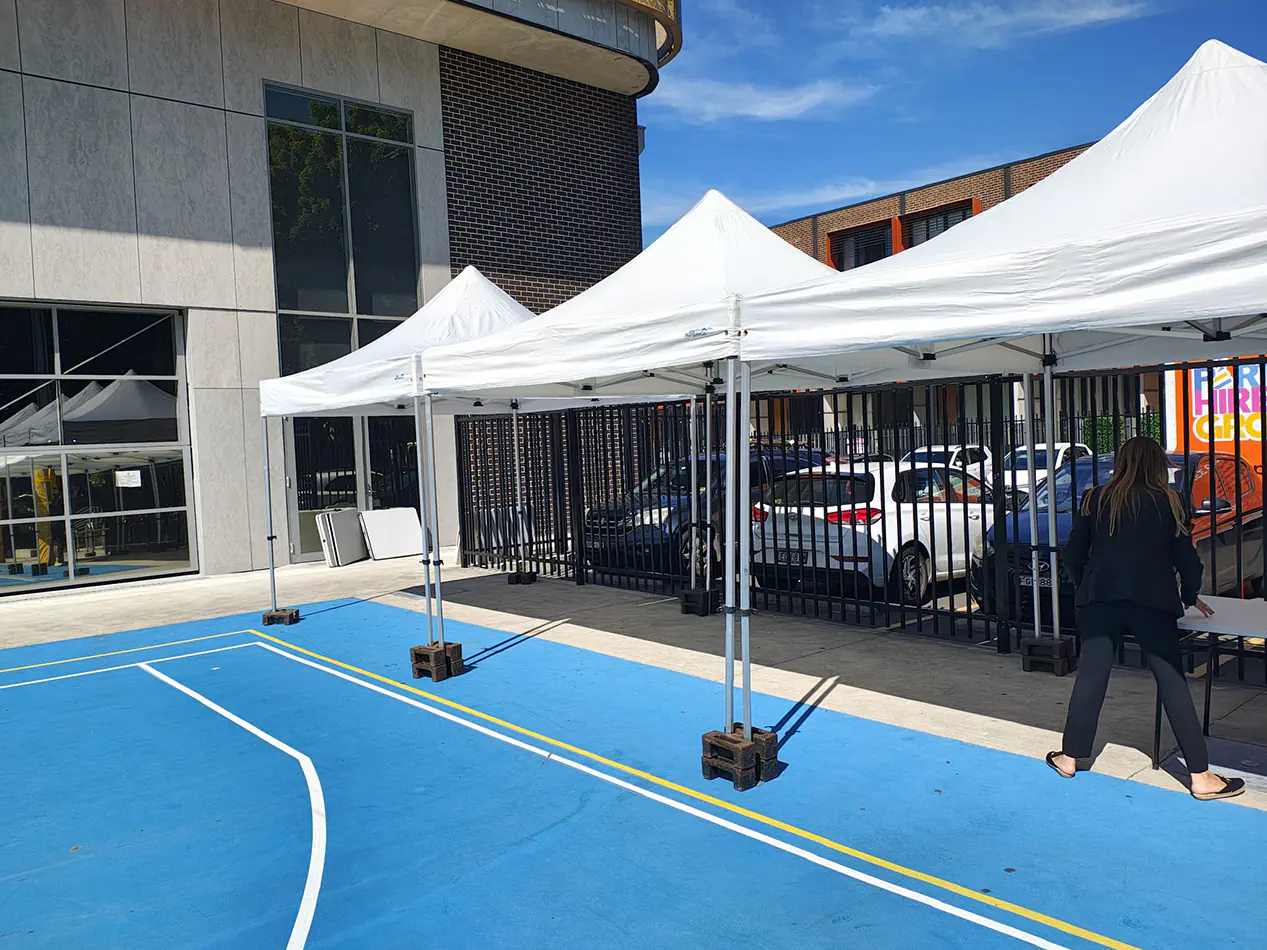 White pop-up marquees set up in a school courtyard for an outdoor event with shade coverage and tables underneath