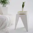 White puzzle stool used as a modern decorative accent in a minimalist indoor space, topped with a small vase of tulips beside a soft white throw and contemporary furnishings.