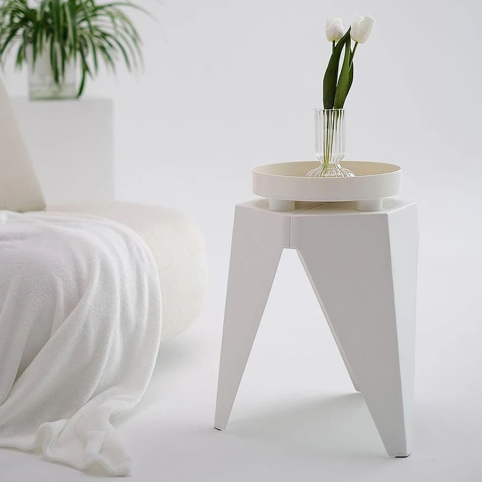 White puzzle stool used as a modern decorative accent in a minimalist indoor space, topped with a small vase of tulips beside a soft white throw and contemporary furnishings.