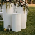 White ripple metal plinths supporting floral arrangements at an outdoor wedding ceremony