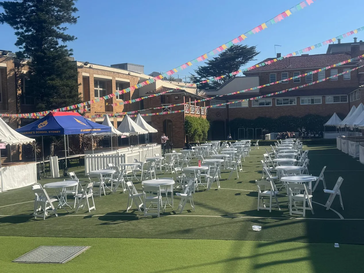 White round café tables with folding chairs arranged across a school lawn for an outdoor event