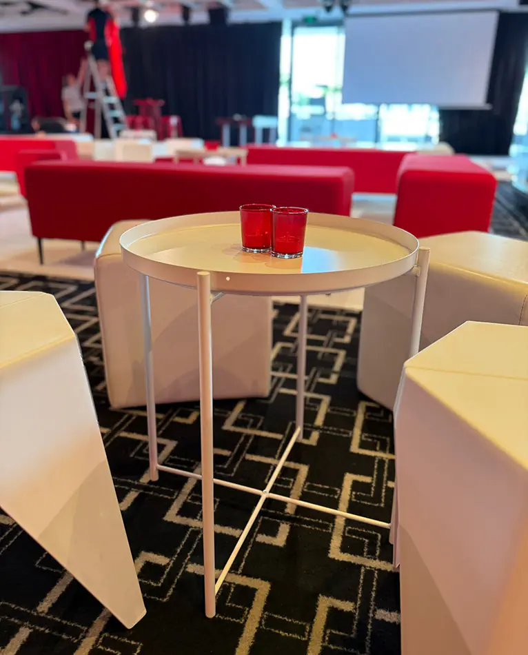 White round side table surrounded by white cube seating and lounge furniture inside a modern corporate event setup