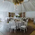 A wedding reception in a white tent with White Tiffany Chair Hire.