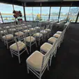White Tiffany chairs arranged for a waterfront wedding ceremony inside a modern function venue overlooking the water