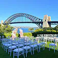 White Tiffany chairs arranged for an outdoor wedding ceremony with Sydney Harbour Bridge and waterfront views in the background