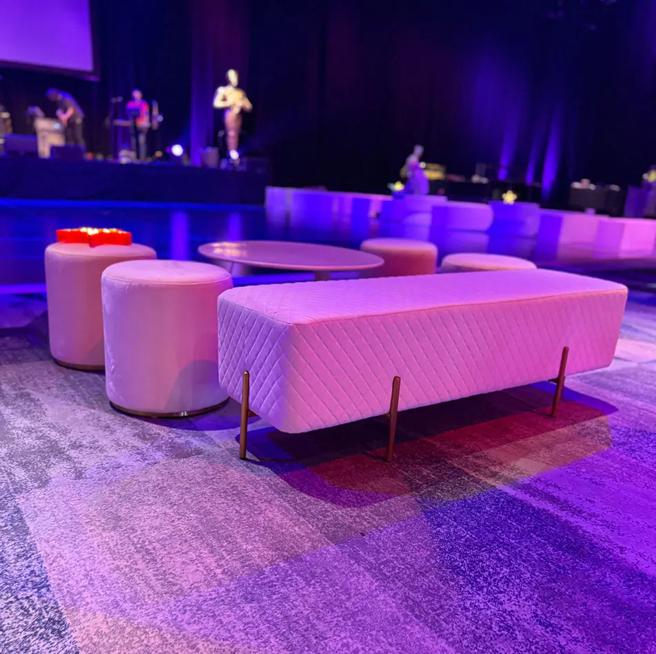 White velvet ottoman bench with matching round stools and low tables styled in a modern event lounge with purple lighting