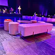 White velvet ottoman bench with matching round stools and low tables styled in a modern event lounge with purple lighting