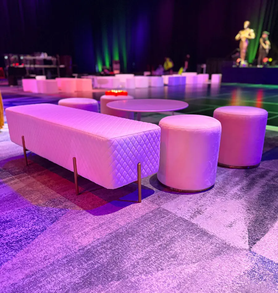 White velvet ottoman stools and quilted bench seating arranged around low tables inside a colourful gala event venue