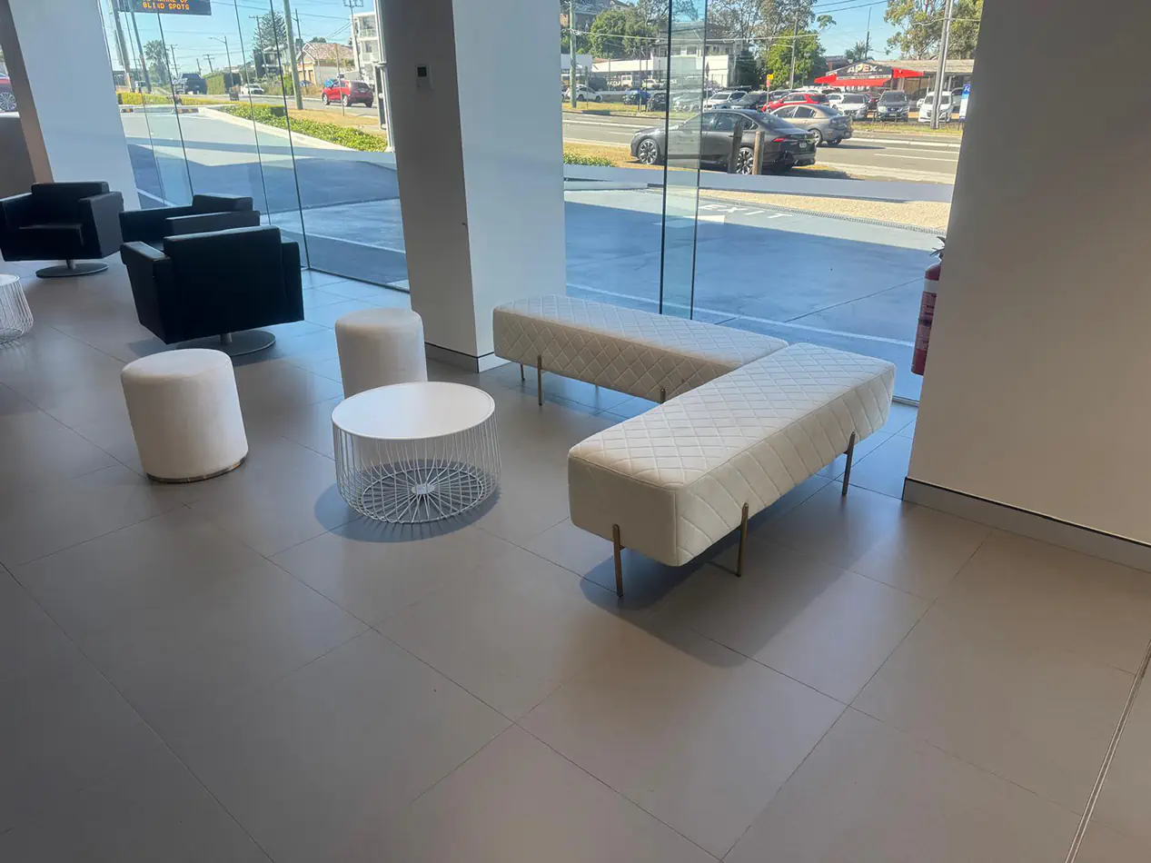 White velvet ottoman stools with quilted lounge seating and white wire coffee table inside a modern showroom lounge area