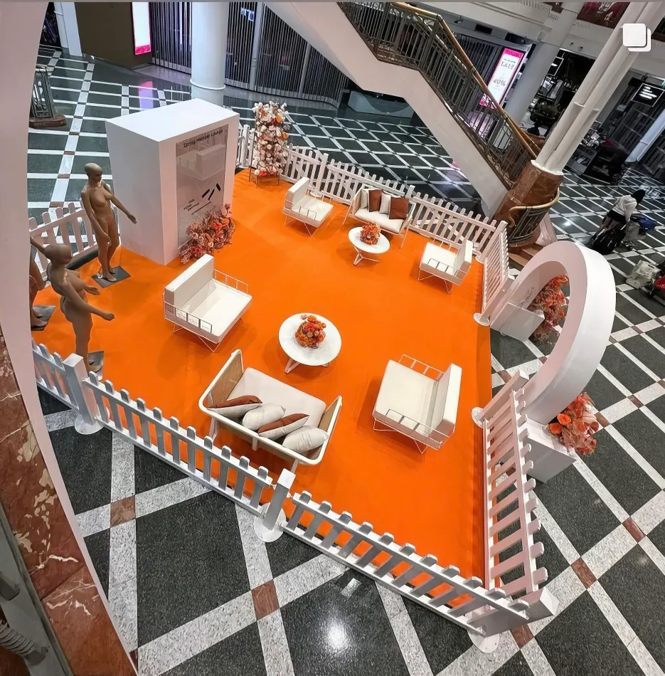 An orange and white display featuring wire arm chair hire with white velvet cushions in a mall.
