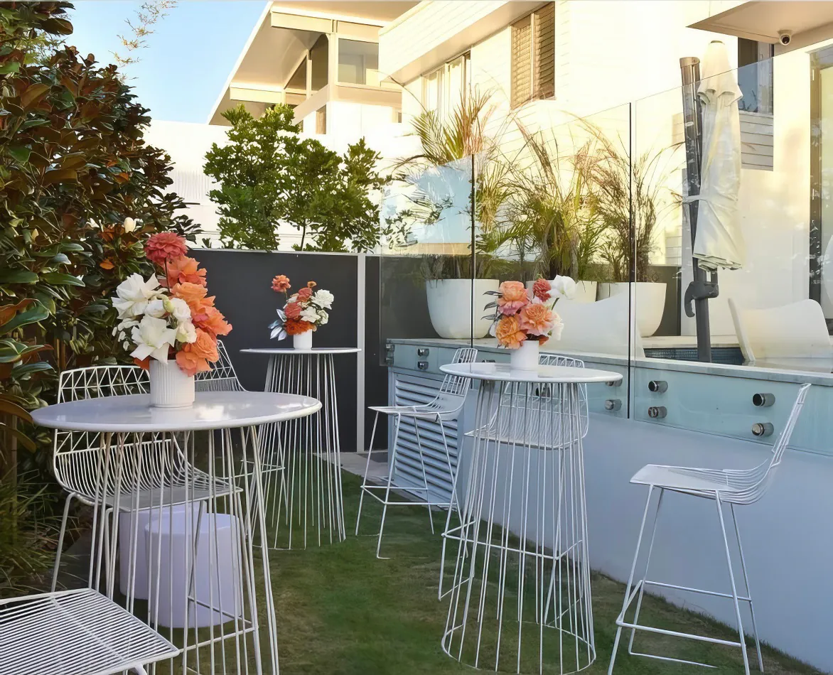 A white table and chairs in a garden, available for white wire cocktail table hire.