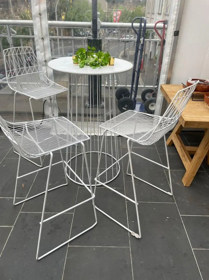 Three white metal chairs and a table on a patio. The patio furniture set includes three chairs and a white table, perfect for outdoor gatherings.