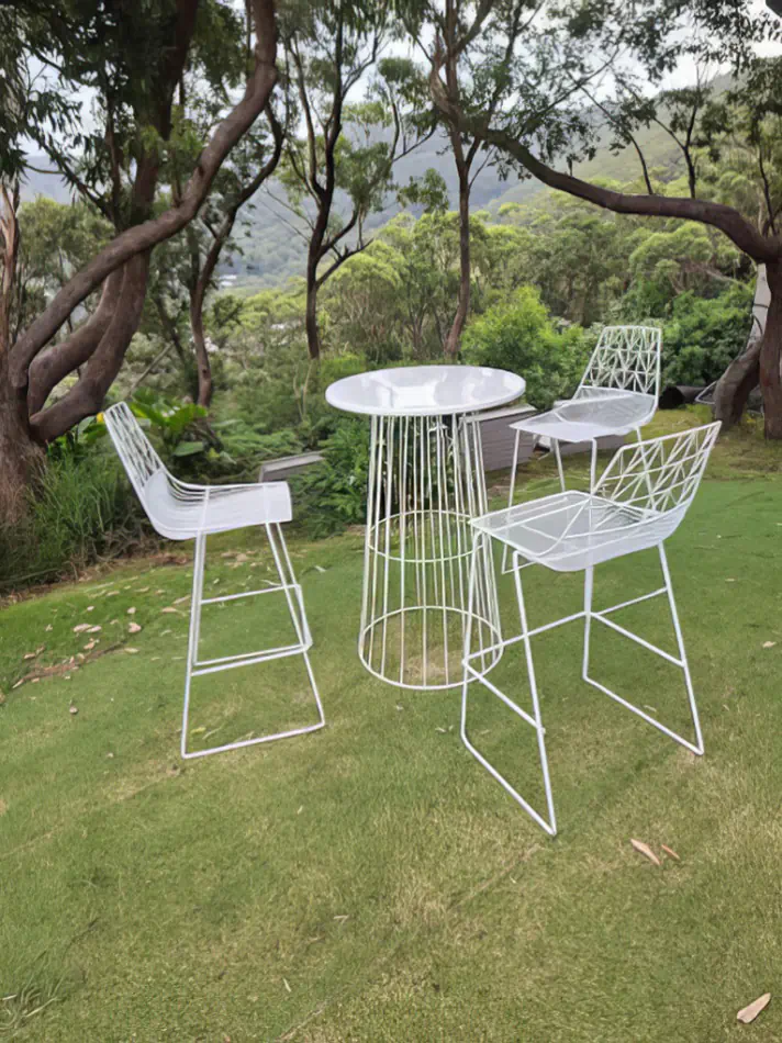 White wire cocktail table hire paired with matching seating set on a grassy outdoor garden location surrounded by trees and natural scenery